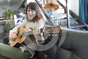 Beauty woman sitting on a dofa and playing guitar