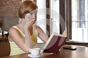 Pretty woman enjoying reading book at coffee shop drinking cup of coffee or tea smiling happy