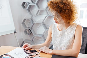 Pretty woman fashion designer choosing models on photos in office