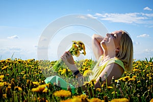 Pretty woman on a field with green grass and yellow dandelion flowers in a sunny day. Girl on nature with yellow flowers and blue