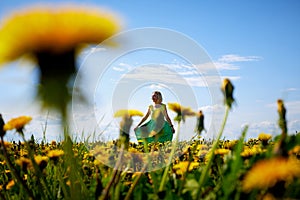 Pretty woman on a field with green grass and yellow dandelion flowers in a sunny day. Girl on nature with yellow flowers and blue