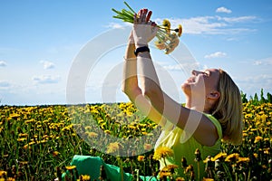 Pretty woman on a field with green grass and yellow dandelion flowers in a sunny day. Girl on nature with yellow flowers and blue