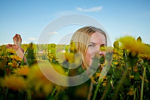 Pretty woman on a field with green grass and yellow dandelion flowers in a sunny day. Girl on nature with yellow flowers and blue