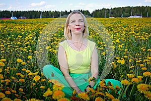 Pretty woman on a field with green grass and yellow dandelion flowers in a sunny day. Girl on nature with yellow flowers and blue