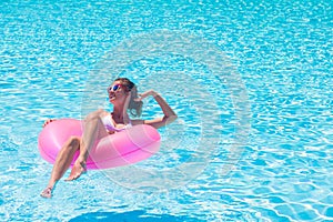 pretty woman floating with pink rubber inflatable ring in swimming pool and having fun