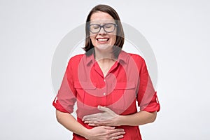 Pretty woman in glasses and red shirt with stomach pain on white background