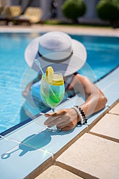 Pretty woman in a hat enjoying cocktail in a swimming pool