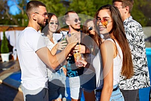 Pretty woman having fun at poolside summer party clinking glasses with friends on sunny summer day near swimming pool