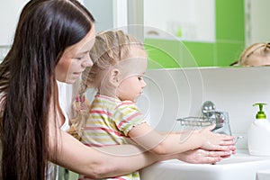 Pretty woman and her daughter kid girl washing hands with soap in bathroom
