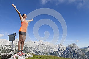 Pretty woman hiker standing on a rock with raised hands