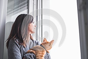 Pretty woman holding a cat and looking out the window