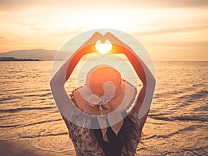 Pretty woman holding hands in heart shape framing setting during sunset on ocean beach