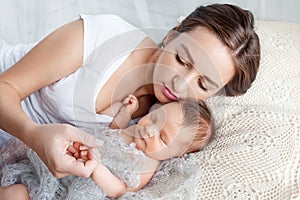 Pretty woman holding a newborn baby in her arms. Happy mother and her slipping newborn baby in the bed