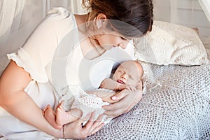 Pretty woman holding a newborn baby in her arms. Happy mother and her slipping newborn baby in the bed