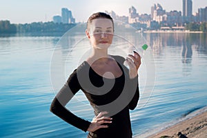 Pretty woman holds water bottle at river and city backround