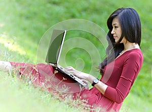 Pretty woman with laptop on green grass at the ga