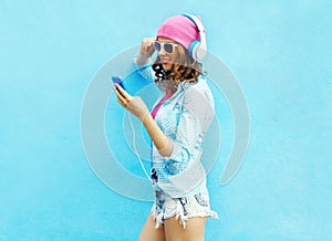 Pretty woman listens to music in headphones using smartphone over colorful blue