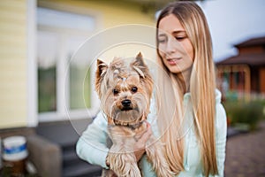 Pretty woman with long blonde hair holding small dog yorkshire terrier outdoor