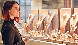 Pretty woman looking at jewelry in store window. Customer near jewellery. Dreamy red hair girl chooses silver, gold, diamonds,