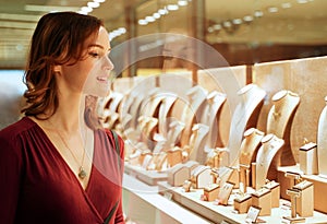 Pretty woman looking at jewelry in store window. Smiling interested customer near jewellery. Girl chooses gold, diamonds or