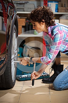 Pretty woman mechanic in overalls tighten the fixing bolts on the wheel of the car