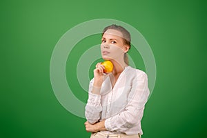 A pretty woman of middle age in a white shirt holds an apple in her hand on a green background. Healthy eating, vegetarianism,