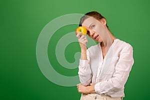 A pretty woman of middle age in a white shirt holds an apple in her hand on a green background. Healthy eating, vegetarianism,