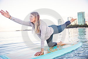 Pretty woman in modified warrior doing SUP Yoga on the water