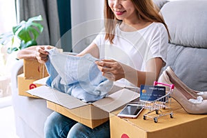 Pretty woman opening boxes of postal parcel with smartphone, parcel boxes, credit card on sofa. Online shopping, e-commerce, new