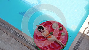 Pretty woman in orange swimsuit lying on inflatable watermelon island in swimming pool