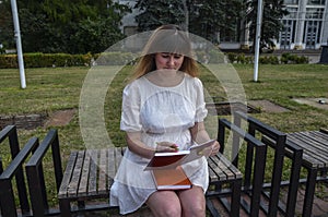 Pretty woman with pen sitting on bench outdoors in nature park and writing on notebook or her diary