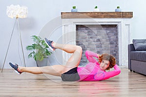 Pretty woman in pink and black sportswear doing exercise on the abdominal muscles lying on the floor