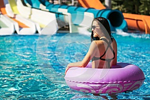 Pretty woman in pink rubber ring in the pool near slide