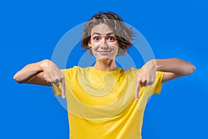 Pretty woman pointing down to advertising area. Blue background. Young lady asking to click to subscribe below. Copy
