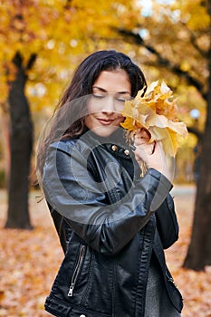 Pretty woman is posing with bunch of maple`s leaves in autumn park. She`s closing eyes and dreaming. Beautiful landscape at fall