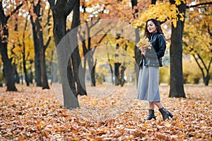 Pretty woman is posing with bunch of maple`s leaves in autumn park. She`s closing eyes and dreaming. Beautiful landscape at fall