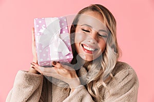 Pretty woman posing isolated over pink wall background holding gift box