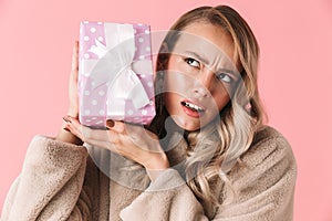 Pretty woman posing isolated over pink wall background holding gift box