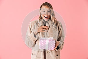 Pretty woman posing isolated over pink wall background holding gift box