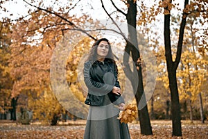 Pretty woman posing with maple`s leaf in autumn park near big tree. Beautiful landscape at fall season