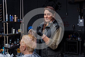 Pretty woman professional barber European at work drying hair with a hair dryer to a client