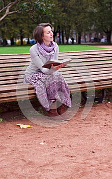 Pretty woman reading a book on bench and thinking