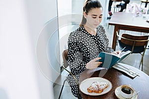 Pretty woman is reading a book in a cafe. Sitting behind round table