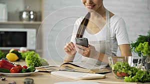 Pretty woman reading cooking book and calculating calories on smartphone app