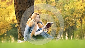 Pretty woman reading interesting book, sitting under tree, spending leisure time