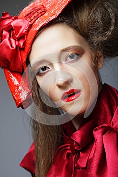 Pretty woman in a red carnival costume and a scarlet hat poses on a gray background.
