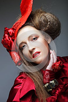 Pretty woman in a red carnival costume and a scarlet hat poses on a gray background.