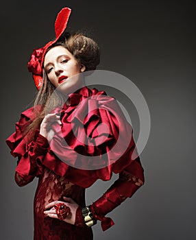 Pretty woman in a red carnival costume and a scarlet hat poses on a gray background.