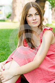 Pretty woman in red dress sitting on park