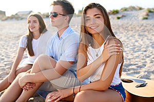 Pretty woman relaxing with friends sitting on beach towel near the sea and sunbathing. Attractive tanned model smiling